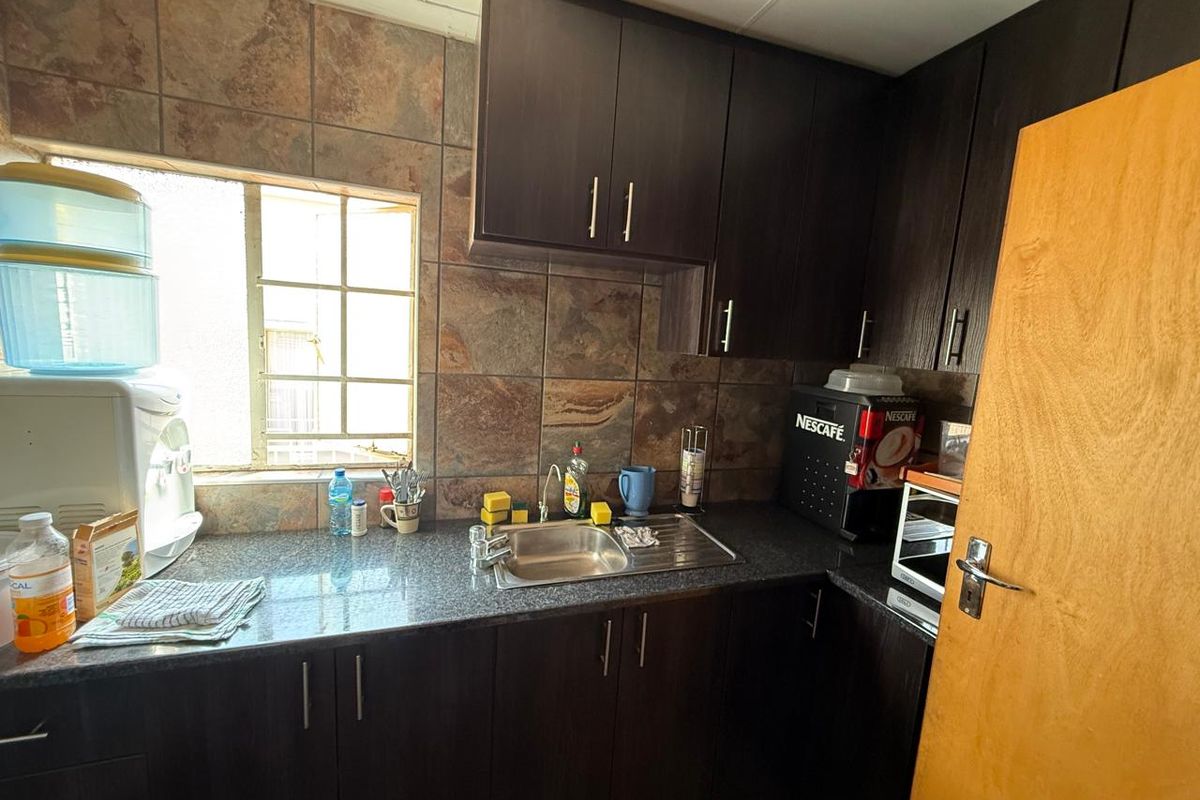Compact office kitchenette featuring dark wood cabinetry, granite-look countertops, stainless steel sink, and stone-style tiled backsplash.