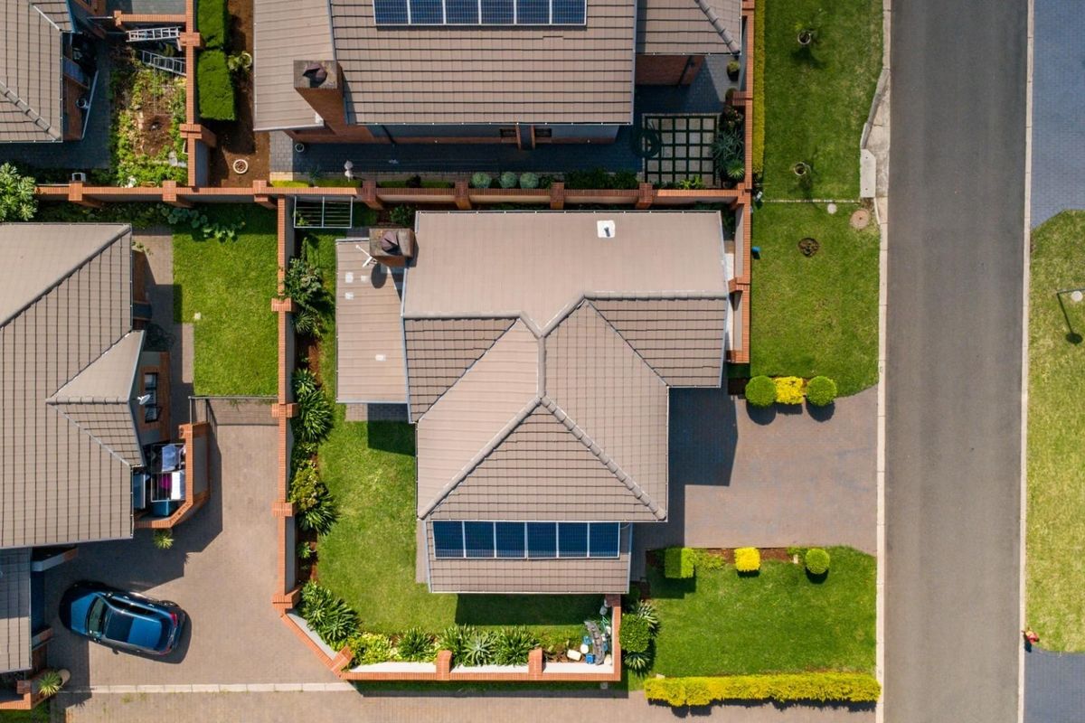 Aerial view of a residential property featuring a tiled roof, integrated solar panels, a paved driveway, and a well-maintained garden.