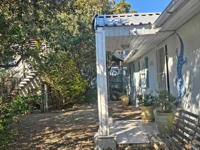 A covered outdoor patio area featuring tiled flooring and timber support posts, providing a shaded entrance space adjacent to the garden.