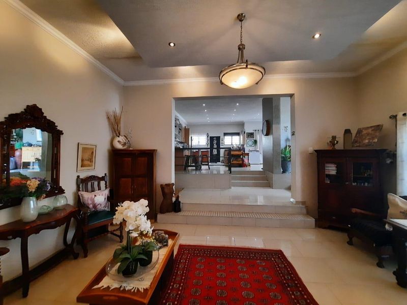 Spacious open-plan living area featuring a multi-level floor design, recessed ceiling with downlights, and neutral tiled flooring connecting to the kitchen space.