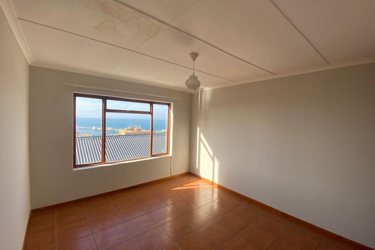 An empty bedroom featuring tiled flooring and a large window with ocean views. The ceiling shows visible signs of water damage.