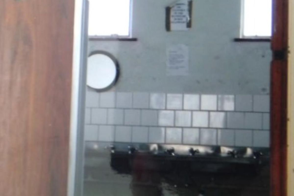 A view into a utilitarian bathroom or washroom area featuring tiled splashbacks and multiple basin fixtures in a dated condition.