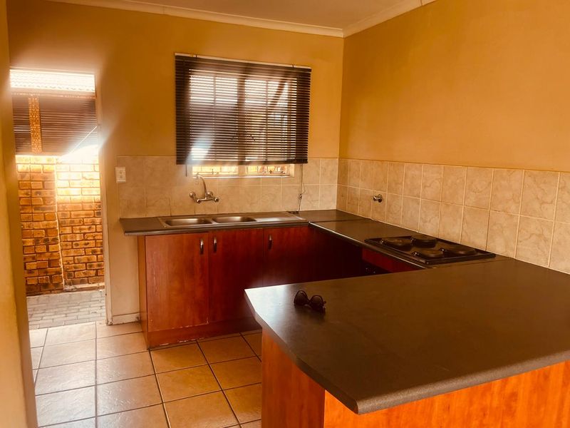 A functional kitchen featuring wooden cabinetry, laminate countertops, a built-in electric hob, and tiled flooring with direct access to an outdoor area.