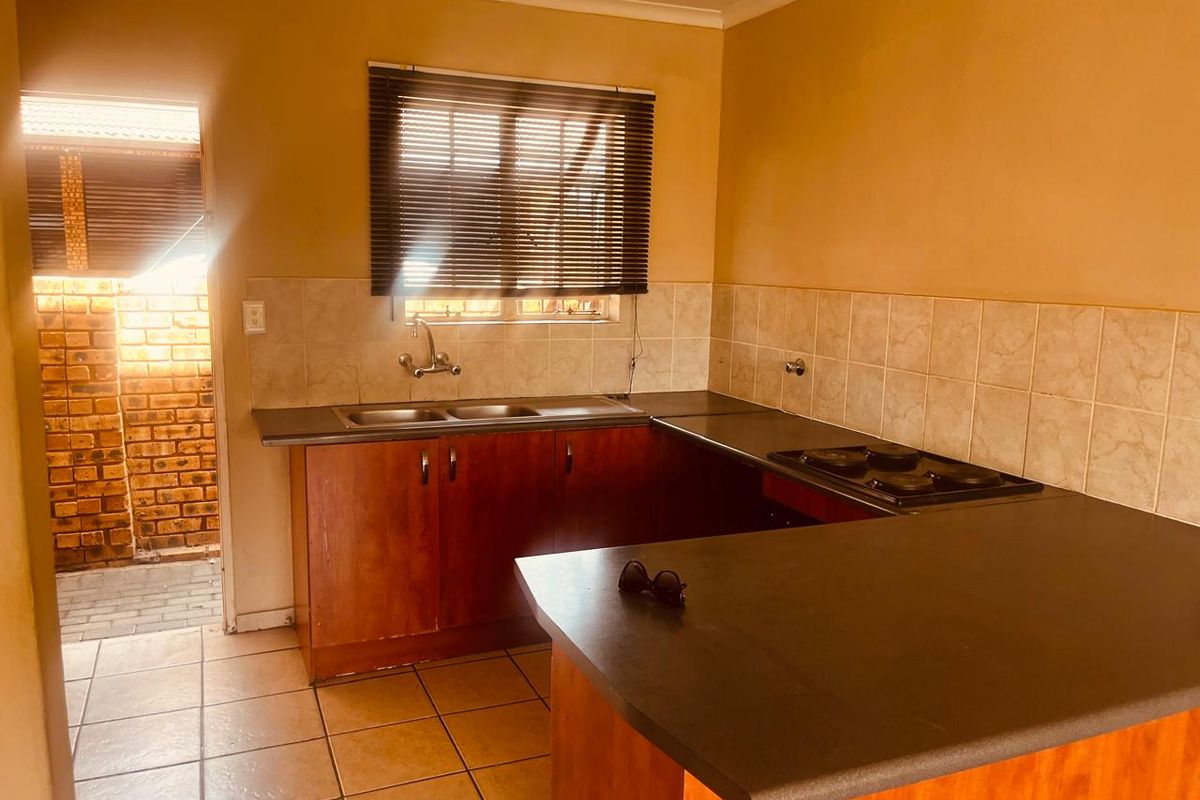 A functional kitchen featuring wooden cabinetry, laminate countertops, a built-in electric hob, and tiled flooring with direct access to an outdoor area.