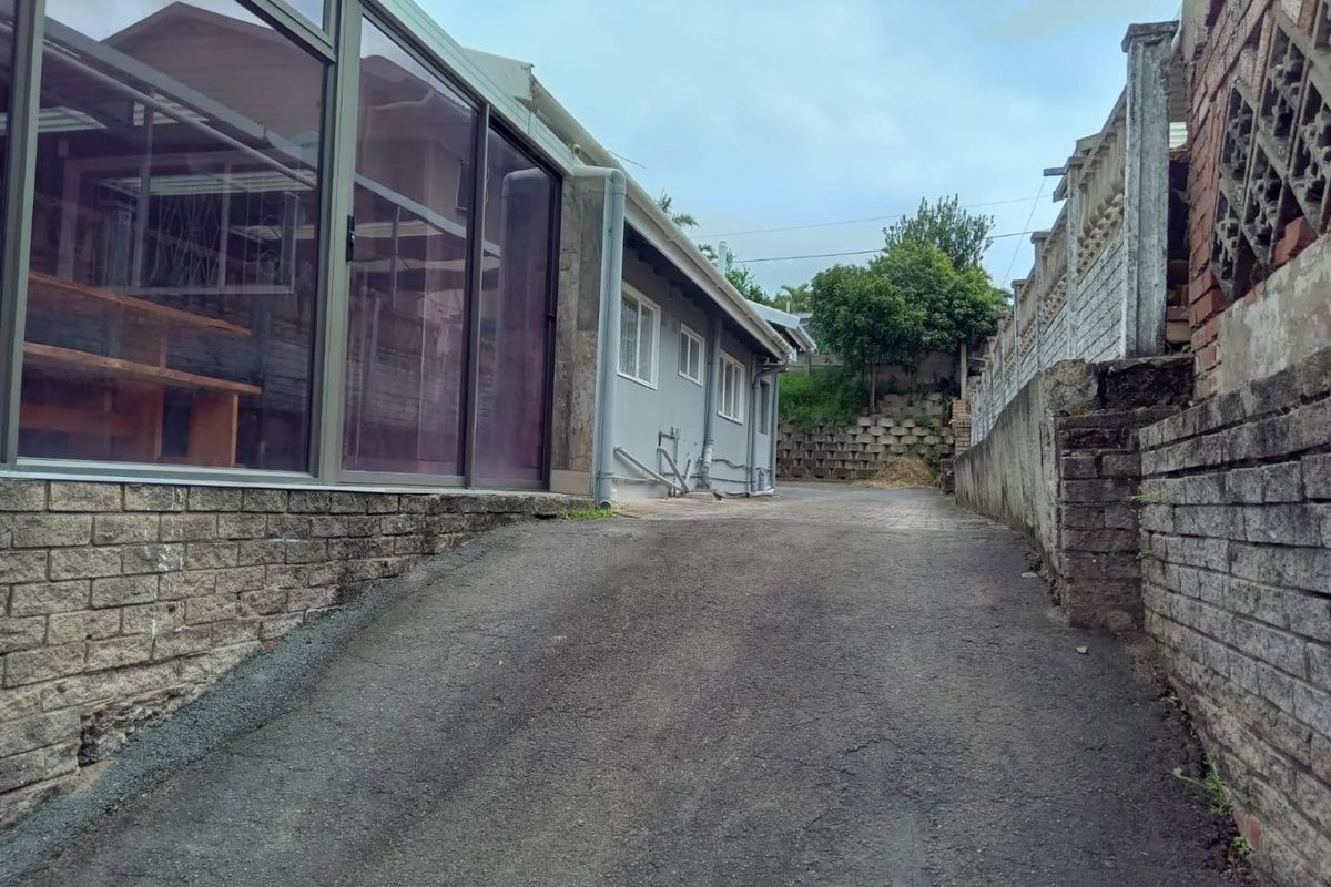 A view of the rear exterior driveway featuring a sloped asphalt surface, retaining walls, and brick boundary fencing alongside the building structure.
