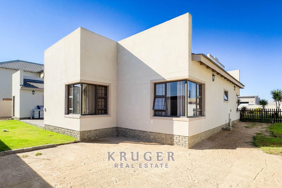 Rear view of the house featuring a modern facade, corner windows, and a surrounding garden area with a sandy yard.