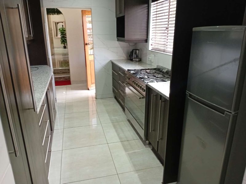 Modern galley-style kitchen featuring dark wood cabinetry, granite countertops, a gas stove, and polished floor tiles.