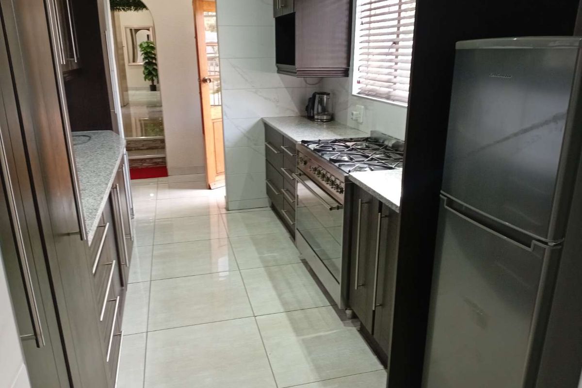 Modern galley-style kitchen featuring dark wood cabinetry, granite countertops, a gas stove, and polished floor tiles.