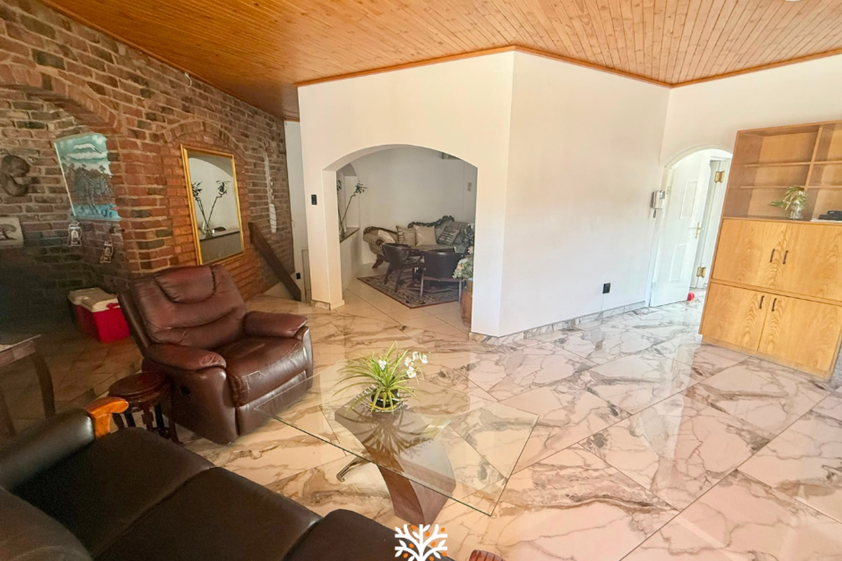 Spacious living area featuring marble-look tiled flooring, a timber-clad ceiling, and an exposed brick feature wall with an arched transition to an adjacent room.