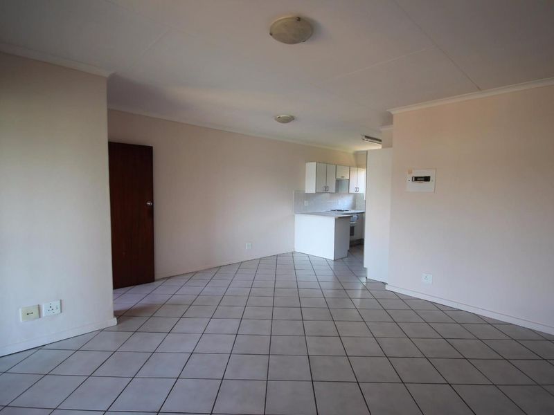An open-plan living area featuring tiled flooring and a compact kitchen with built-in cabinetry and a cooktop.