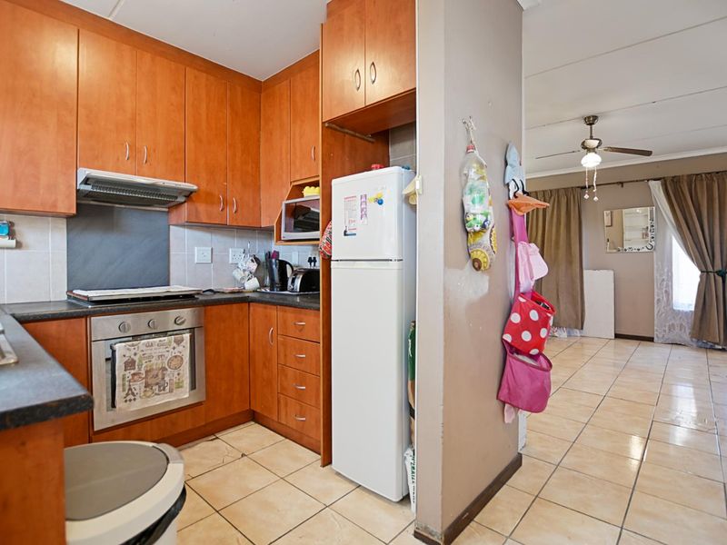 Open plan kitchen featuring wood-finish cabinetry, built-in oven, and extractor fan, flowing into an adjacent living area with tiled flooring throughout.