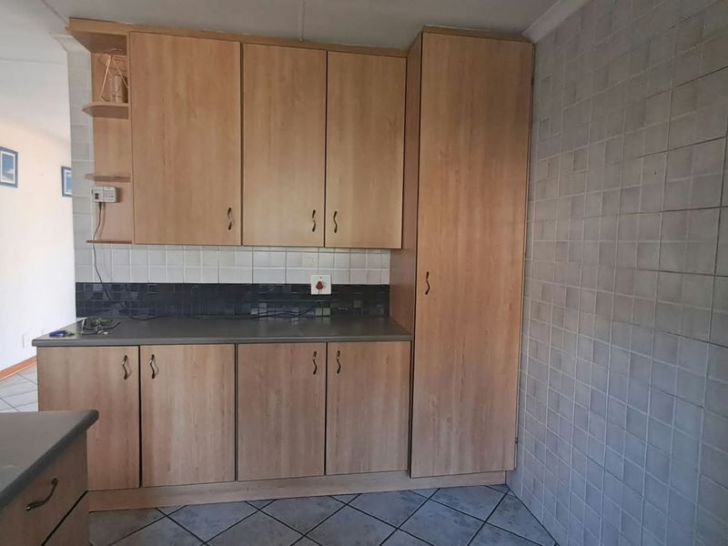 A functional kitchen area featuring light wood-finish cabinetry, dark laminate countertops, a tiled backsplash, and neutral floor tiles.