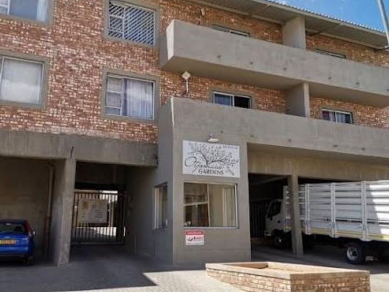 Front elevation of a multi-story townhouse complex featuring brick facade, concrete balconies, and a paved entrance area with security access.