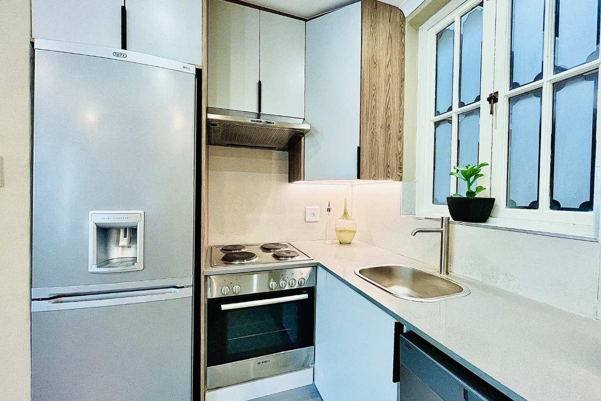 Compact modern kitchen featuring sleek cabinetry, stone countertops, stainless steel oven, electric hob, extractor fan, and a stainless steel sink.