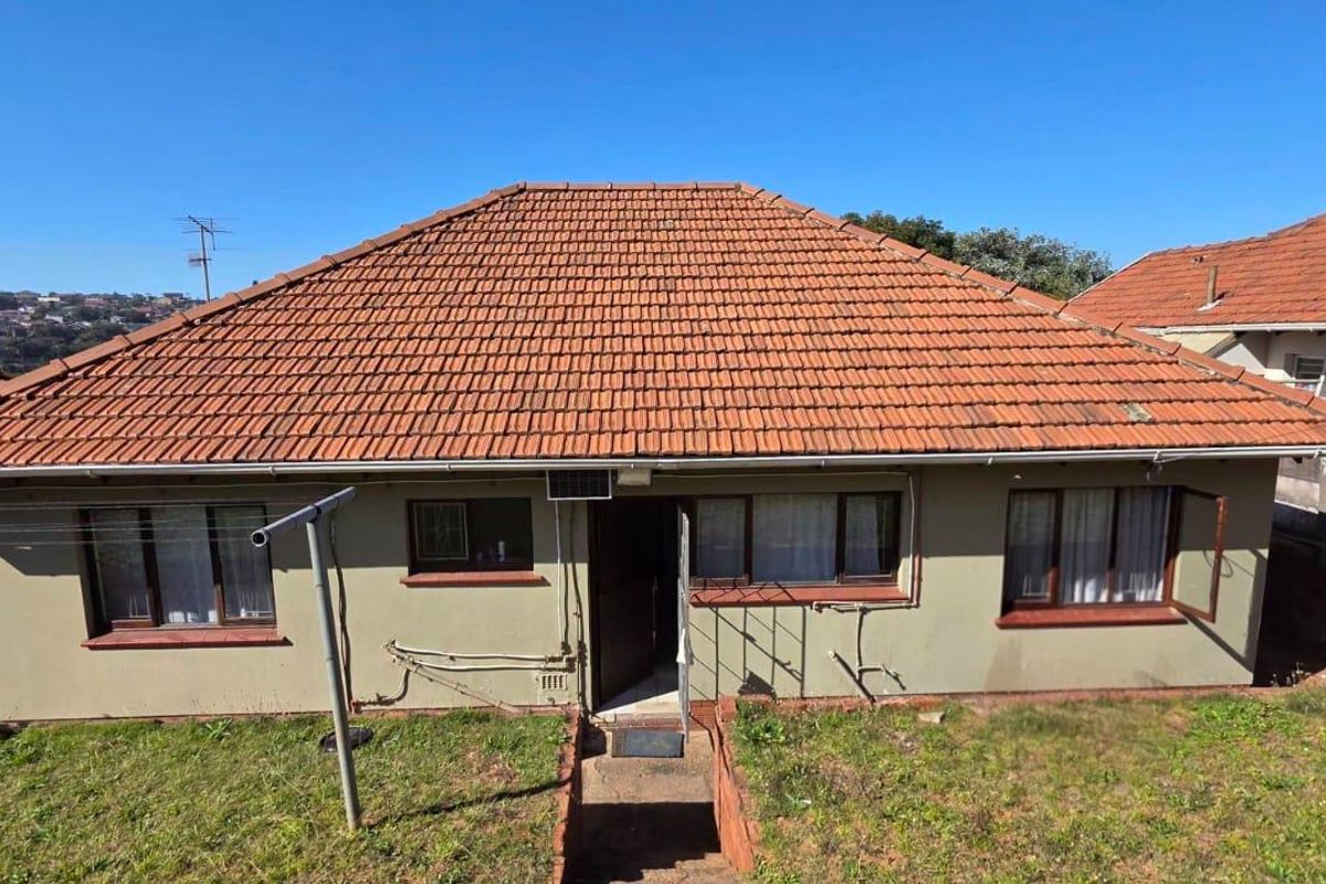 Rear view of a single-story house featuring a terracotta tiled roof, plastered exterior walls, and metal-framed windows.