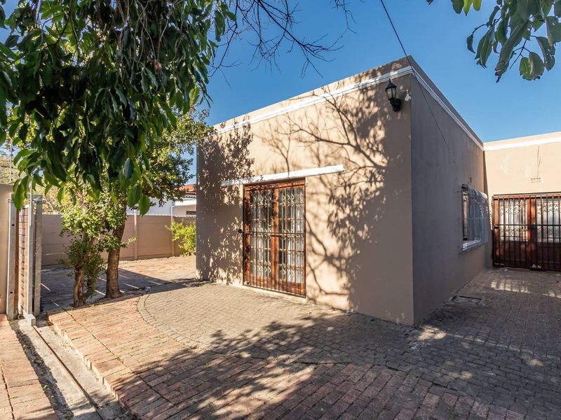 A rear exterior view of the property featuring a paved courtyard area, secure metal gates, and perimeter boundary walls.