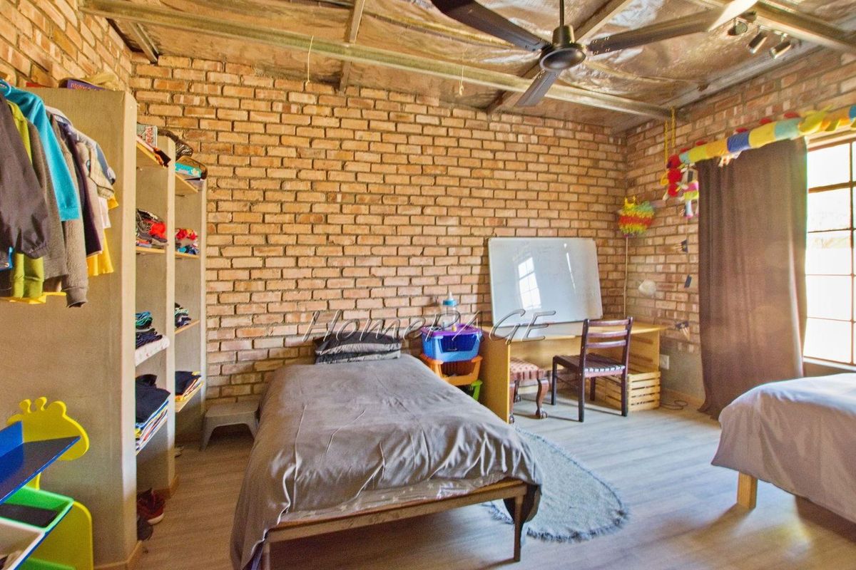 A bedroom featuring exposed brick walls, laminate flooring, and an industrial-style exposed ceiling with a fitted fan.