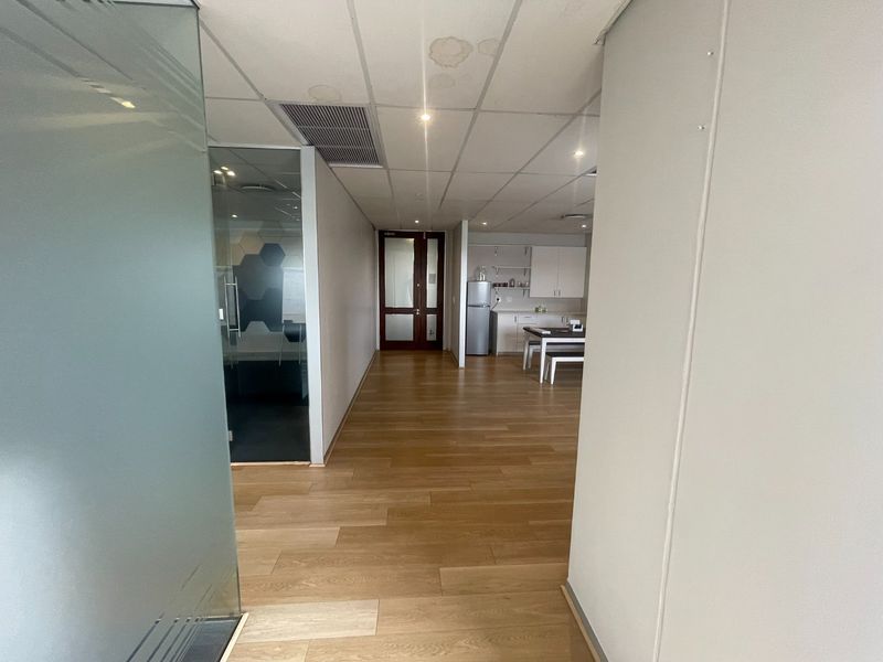 Open plan office space featuring laminate flooring, a glass-partitioned meeting room, and a small kitchenette area with built-in cabinetry.