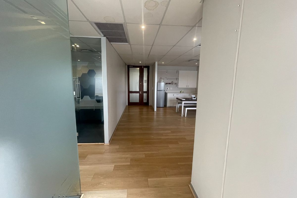 Open plan office space featuring laminate flooring, a glass-partitioned meeting room, and a small kitchenette area with built-in cabinetry.