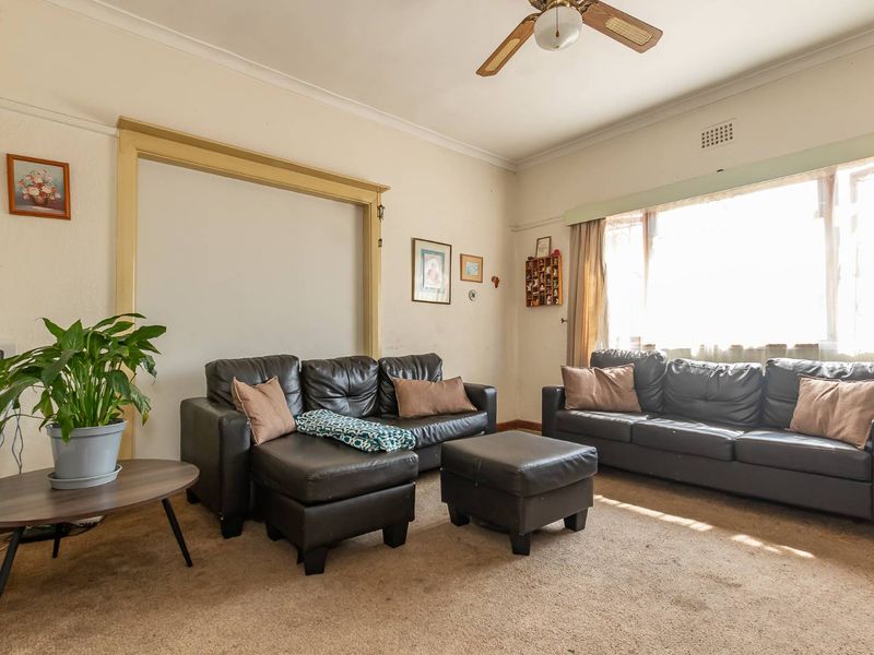 A living room featuring a ceiling fan, large window, and carpeted flooring, presenting an opportunity for cosmetic updates to modernize the space.