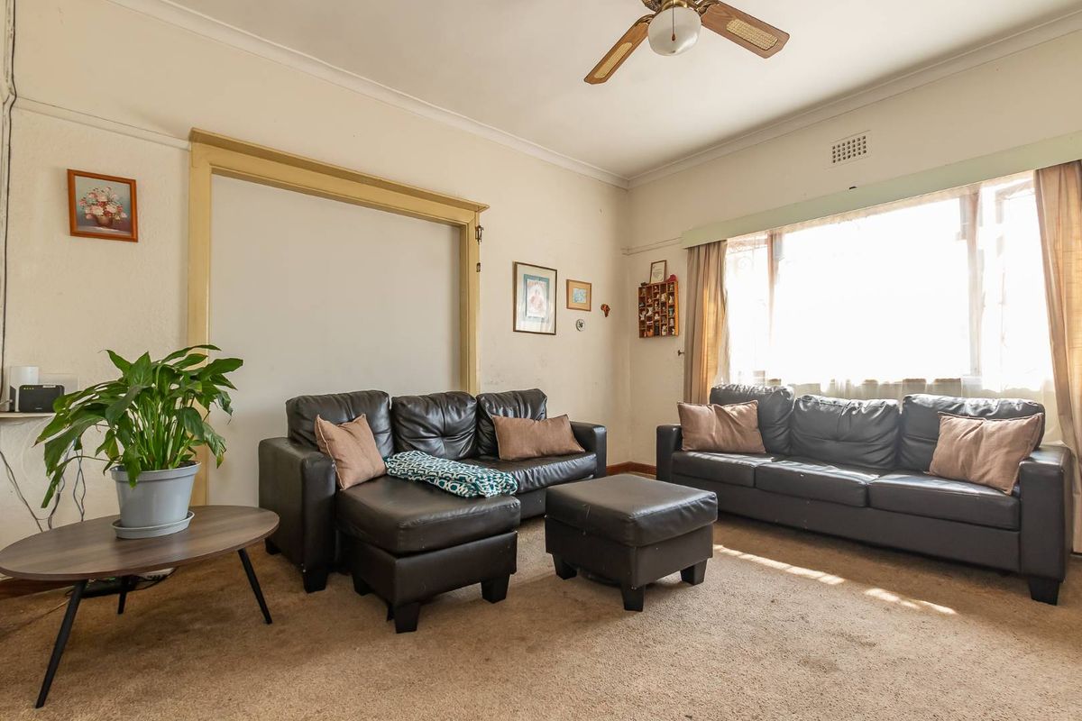 A living room featuring a ceiling fan, large window, and carpeted flooring, presenting an opportunity for cosmetic updates to modernize the space.