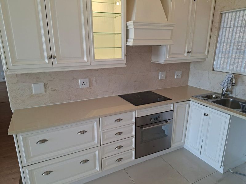 A well-maintained kitchen featuring white cabinetry, stone countertops, a built-in oven, electric hob, and a tiled backsplash.