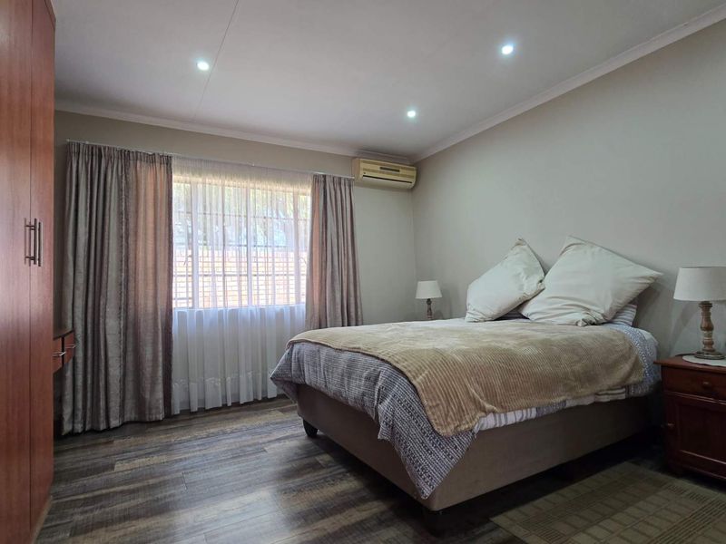 A well-maintained bedroom featuring laminate flooring, built-in wardrobe storage, recessed downlighting, and a wall-mounted split-system air conditioning unit.