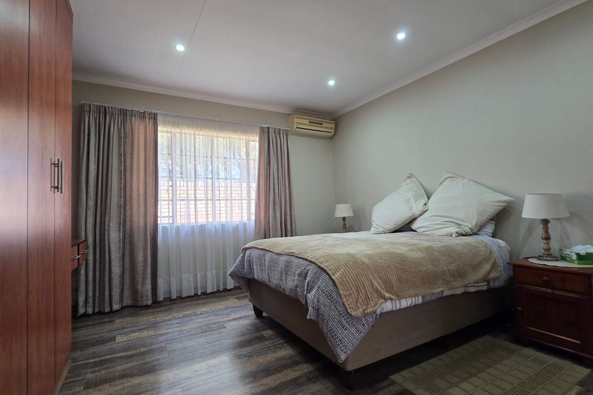 A well-maintained bedroom featuring laminate flooring, built-in wardrobe storage, recessed downlighting, and a wall-mounted split-system air conditioning unit.