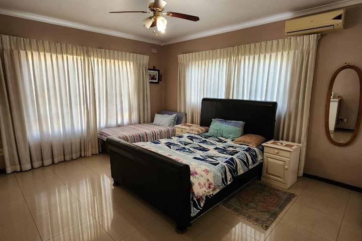 Spacious bedroom featuring tiled flooring, a ceiling fan, and a wall-mounted split-system air conditioner.