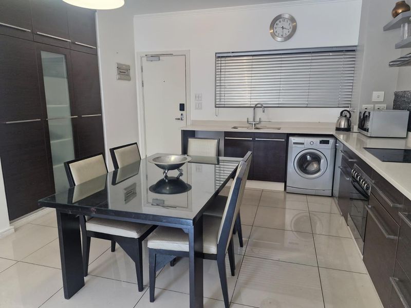 Modern open-plan kitchen and dining area featuring dark wood cabinetry, sleek countertops, integrated appliances, and polished floor tiles.