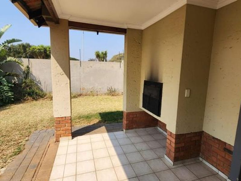A covered patio area featuring tiled flooring, brick-accented pillars, and a built-in braai, overlooking a private garden space.