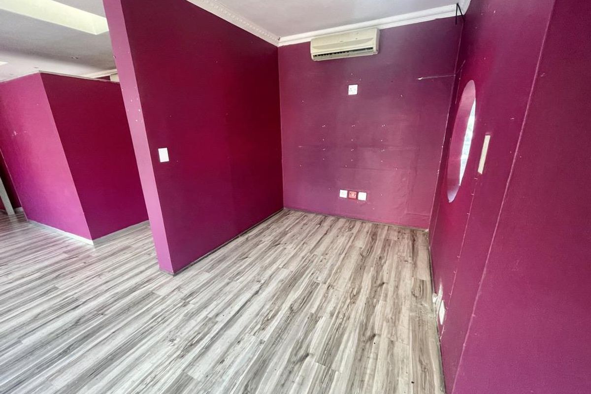 An empty room featuring wood-look laminate flooring, a wall-mounted air conditioning unit, and a distinctive circular window.