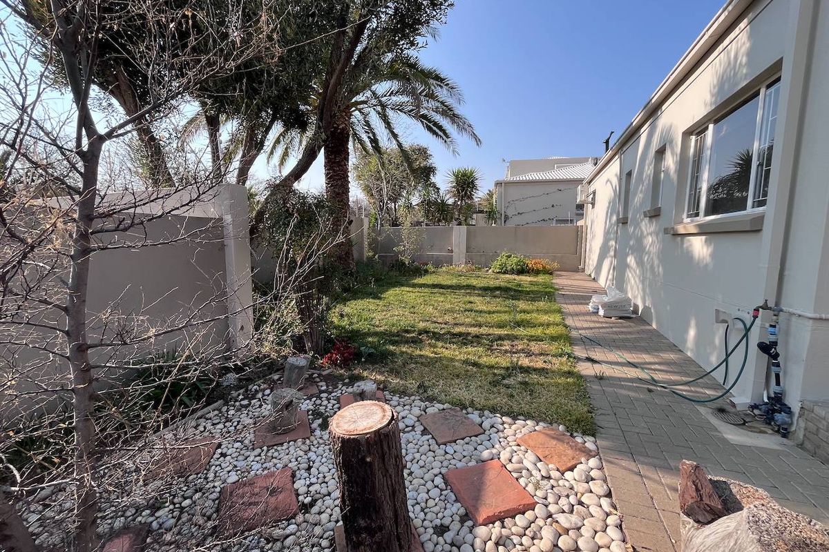 A private rear garden featuring a paved walkway, landscaped pebble area with stepping stones, and perimeter boundary walls.