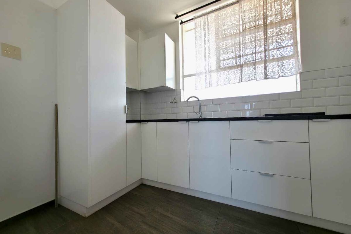 A clean, modern kitchen featuring white cabinetry, dark countertops, and classic subway tile backsplash with a functional sink and window.