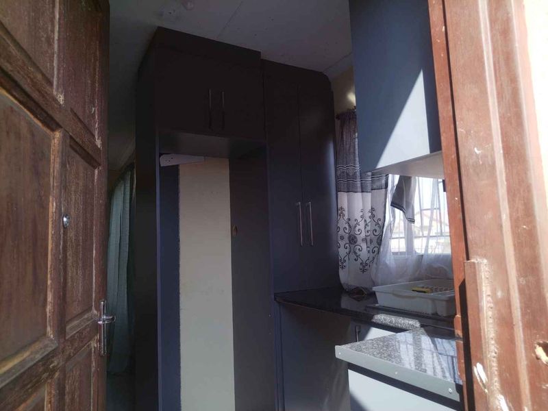 A compact kitchen area featuring dark built-in cabinetry and granite countertops, viewed through a wooden doorway.