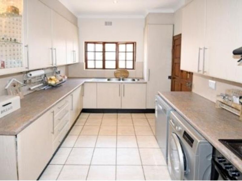 A functional kitchen featuring laminate countertops, ample built-in cabinetry, a double bowl sink, and tiled flooring with integrated cooking appliances.