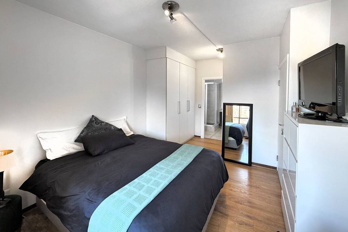 A well-lit bedroom featuring built-in wardrobes, laminate wood flooring, and an en-suite bathroom access.