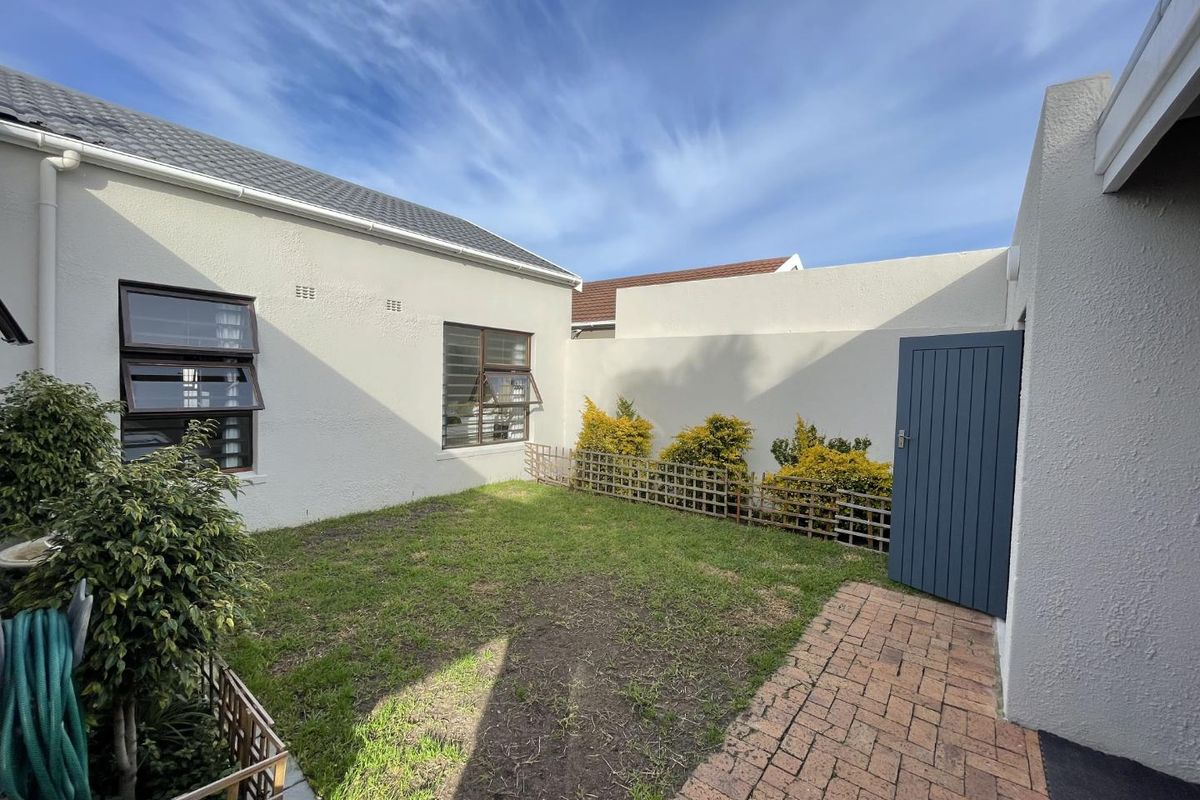 A private rear courtyard featuring a paved walkway, small lawn area, and secure boundary walls with a timber access gate.