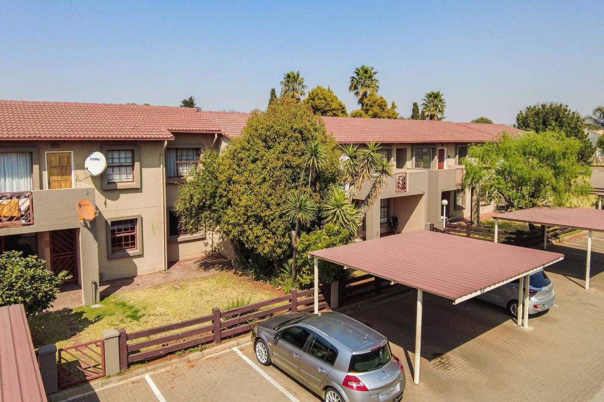 Aerial view of an apartment complex featuring tiled roofing, covered parking bays, and established garden areas.