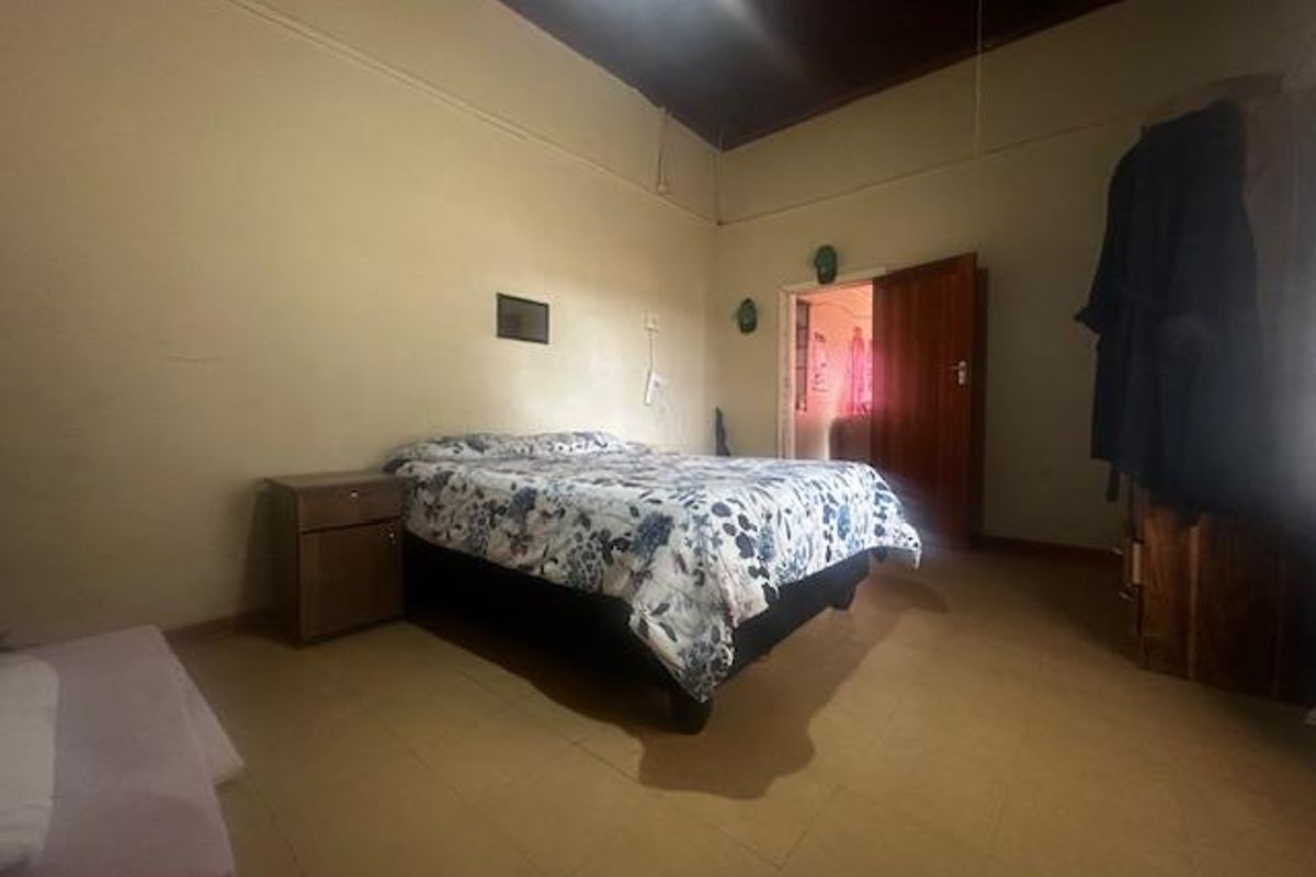 A spacious bedroom featuring high ceilings, tiled flooring, and a traditional wooden door, offering a blank canvas for potential interior updates.