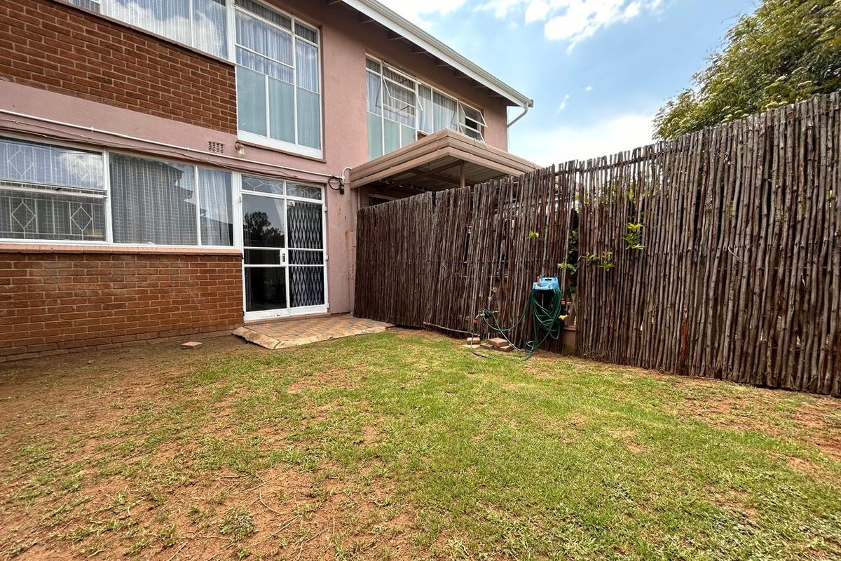 A private rear garden area featuring a small lawn, paved patio section, and rustic timber fencing attached to the townhouse exterior.