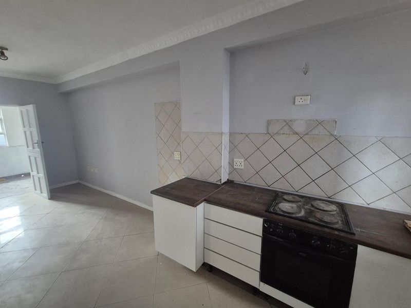 An empty kitchen area featuring built-in cabinetry, an integrated oven and hob, and tiled backsplash, offering a blank canvas for renovation.