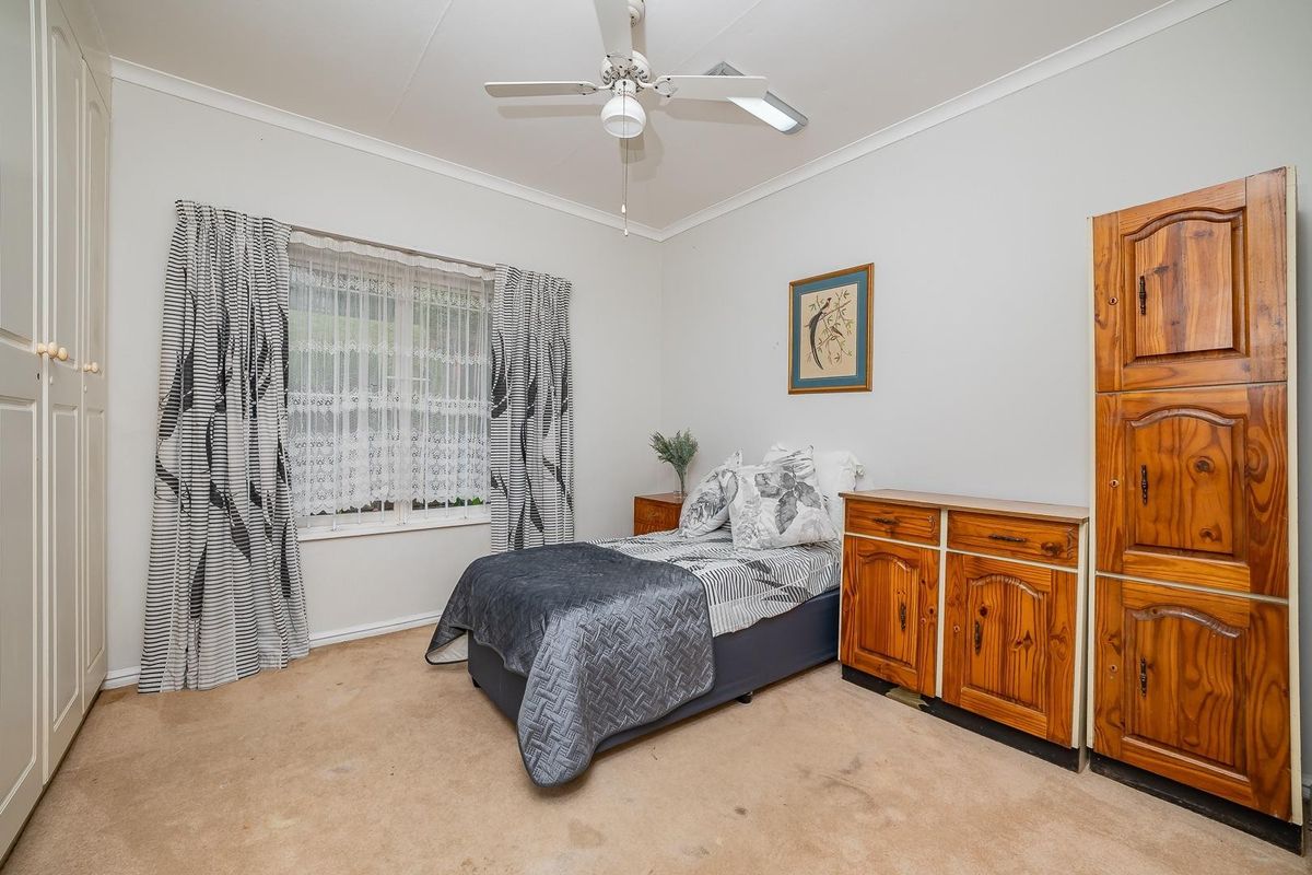 A bedroom featuring built-in wardrobes, a ceiling fan, and carpet flooring, offering a functional space with potential for cosmetic updates.