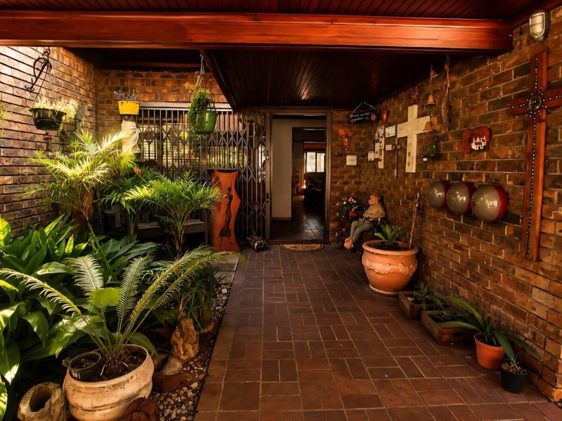 A covered patio area featuring exposed brick walls, timber ceiling, and paved flooring, providing a sheltered entrance to the home.