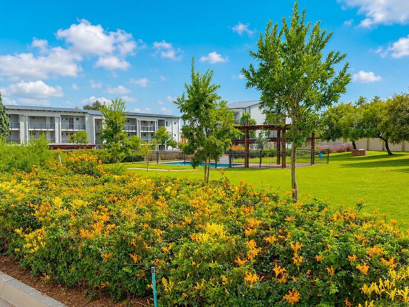 A well-maintained communal outdoor area featuring a swimming pool, pergola, and landscaped gardens within the apartment complex grounds.