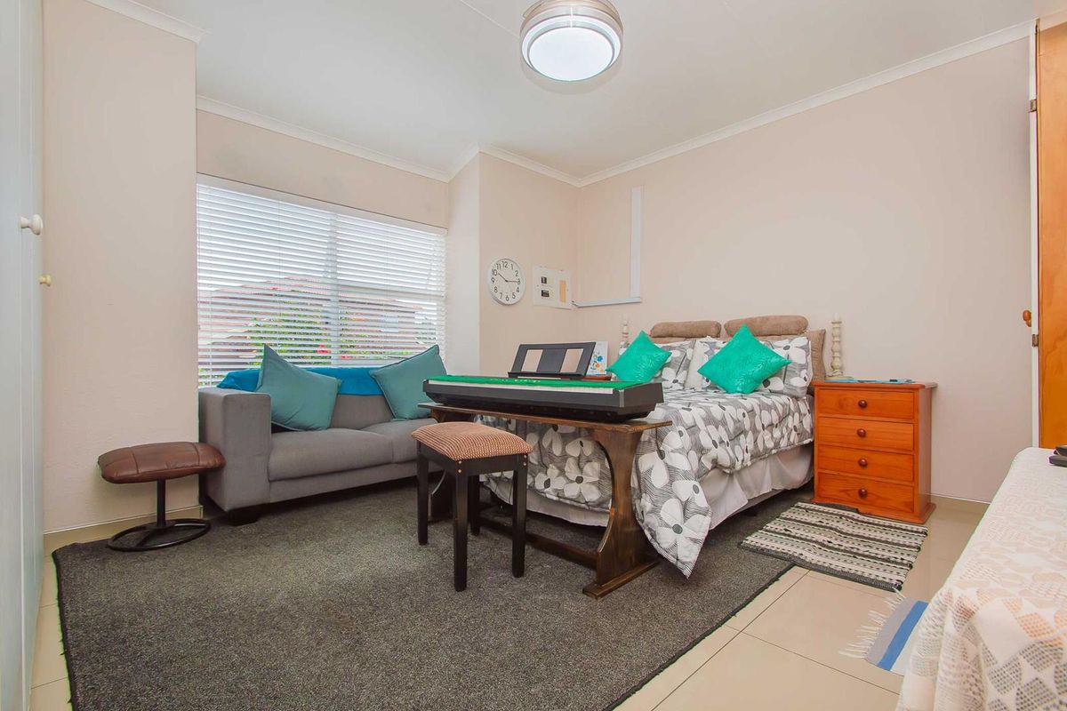 A well-lit bedroom featuring tiled flooring, neutral wall finishes, and a large window with fitted blinds.