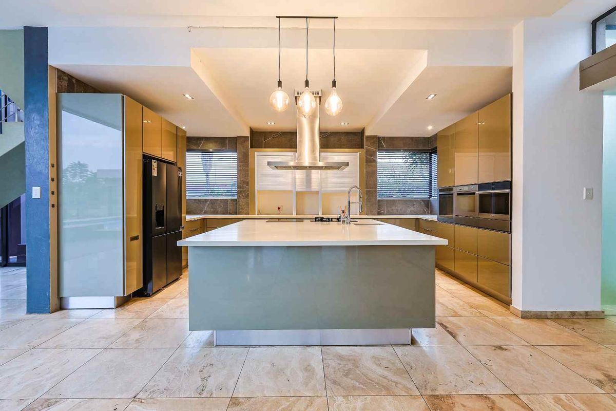 Modern kitchen featuring a large central island, high-gloss cabinetry, integrated double ovens, stainless steel extractor fan, and stone-tiled flooring.
