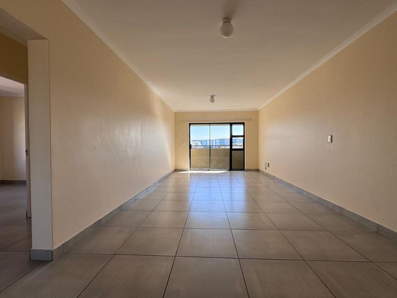 A spacious, empty living area featuring neutral tiled flooring, plain walls, and a sliding glass door leading to an outdoor balcony.