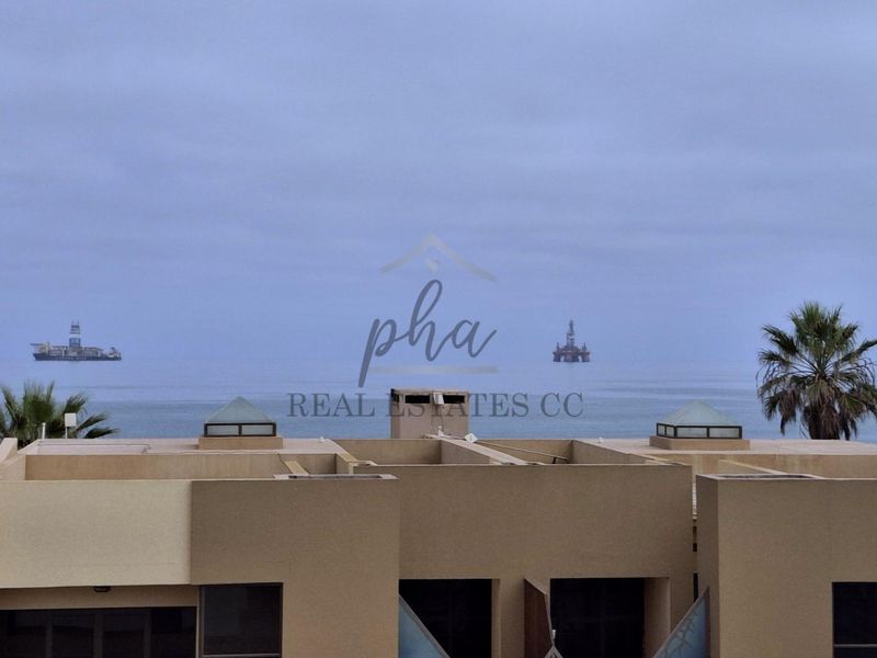 An elevated view overlooking the ocean, featuring the building's roofline with skylights and parapet walls under an overcast sky.