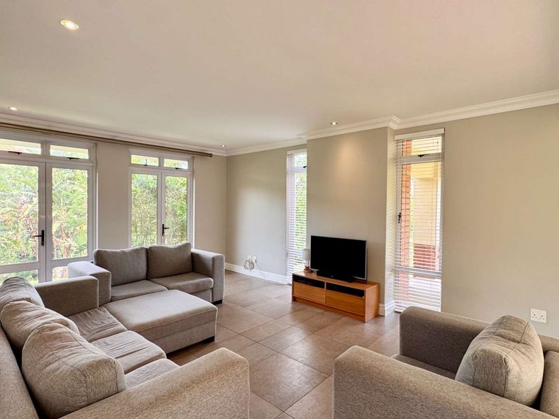 A bright and spacious living room featuring neutral tiled flooring, recessed downlights, and multiple sets of french doors providing ample natural light.